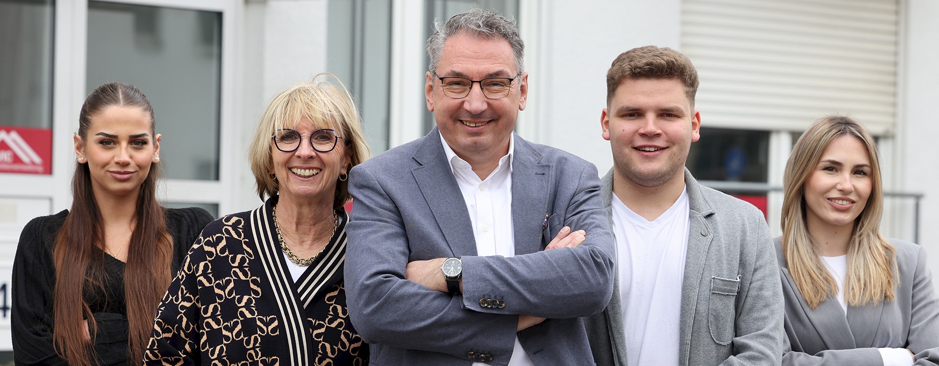 Ein-Team-aus-zwei-Maennern-und-drei-Frauen-steht-laechelnd-vorm-Eingang-eines-Bueros-fuer-Hausverwaltungen-in-Karlsruhe